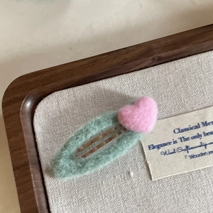 Detailed macro of a handmade wool felt heart hair clip with green oval base and pink heart