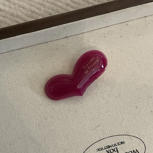 French style heart-shaped magenta hair clip with golden script on cream canvas background