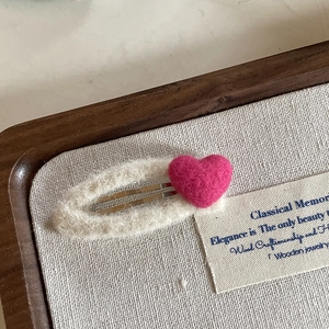 Close-up of a cute handmade pink felt heart hair clip on a soft cream plush base