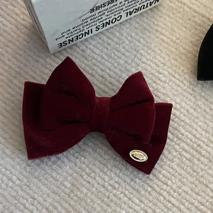Pinza de pelo con lazo de terciopelo rojo oscuro y emblema dorado sobre fondo de punto