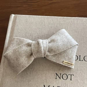Detailed macro view of a beige felt bow hair clip featuring a gold handmade metal tag