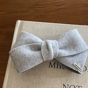 Elegant grey handmade bow hair clip with silver metal tag on a minimalist wooden surface