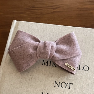 Handmade mauve felt bow hair clip with gold metal tag on a rustic linen book cover