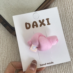 Détail d'une pince à cheveux en tissu rose avec étiquette arc-en-ciel sur carte