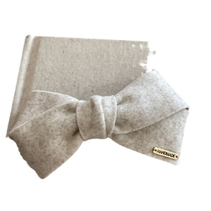 Beige felt bow hair clip with a gold handmade metal tag shown from a side view