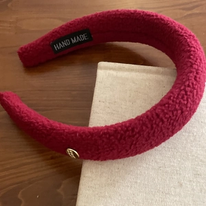 Detail of red textured fabric headband with golden metal charm and handmade label