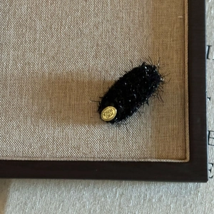 Detail of plush black hair clip with golden metallic brand tag on textured fabric