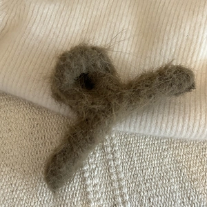 Dettaglio di un grande fermaglio per capelli in peluche grigio scuro su maglia bianca