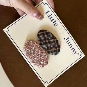Detailed macro view of two oval tweed hair clips in pink and brown patterns on a card