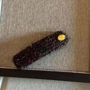 Brown fuzzy plush hair clip with gold metal oval logo detail on linen background