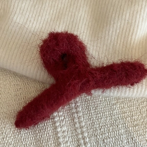 Dettaglio di un mollettone in peluche bordeaux su tessuto testurizzato crema