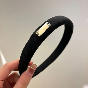 Detail of a black fabric headband with a sleek gold rectangular metal plate accent