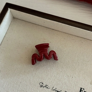 Petite pince à cheveux rouge bordeaux ondulée sur un plateau de présentation épuré