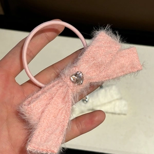 Pink fluffy bow hair scrunchie with a heart crystal detail held in a close-up shot