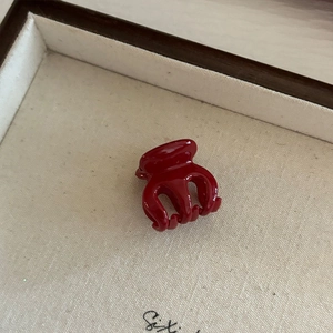 Gros plan d'une mini pince à cheveux rouge foncé brillant sur un plateau à bijoux beige
