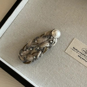 Detail of tweed hair clip with silver chains and a large white pearl embellishment