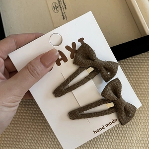 Detail showing two brown textured fabric bow clips with subtle glitter on display card