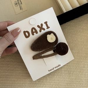 Close-up of brown velvet hair clips with a cute bear patch and plush ball on a card