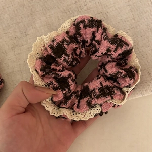 Pink and brown houndstooth tweed scrunchie with cream lace trim detail held in hand