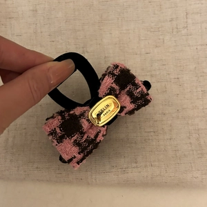 Close-up of pink tweed bow hair tie with a gold metal plate and black elastic band