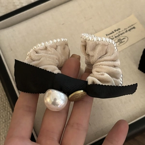 Close-up of beige velvet hair tie with pearl edges and a black grosgrain bow accessory