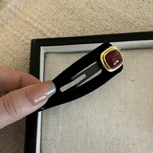 Macro detail of retro black matte BB hair clip with red gemstone and gold square border