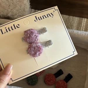 Close-up of cute purple plush ball hair clips with silver glitter details on a display card