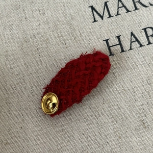 Detail of red tweed hair clip with textured weave and gold button decoration