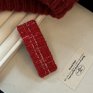 Close-up of red tweed hair clip featuring vintage frayed edges and textured woven fabric