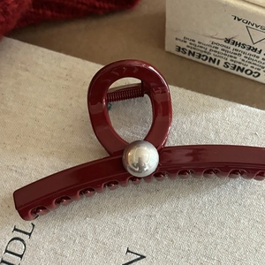Pince à cheveux rouge vin élégante avec perle argentée sur fond en tissu beige texturé