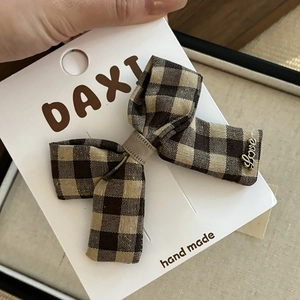 Détail d'une pince à cheveux à nœud écossais marron avec pendentif Love doré