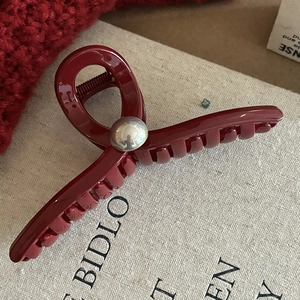 Vue détaillée d'une pince à cheveux rouge brillant avec perle argentée sur fond en lin