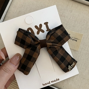 Détail d'un nœud papillon à carreaux marron avec un pendentif Love doré sur carte