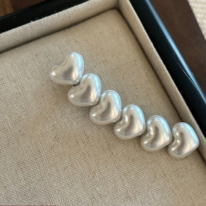 Eleganter cremeweißer Perlenhaarclip mit sechs herzförmigen Perlen auf einem Leinenkissen