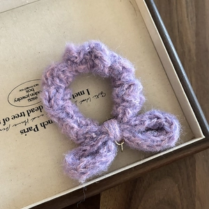 Chouchou en laine tricotée violette avec nœud en peluche dans un plateau en bois