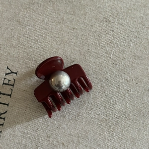Vue macro d'une pince à cheveux bordeaux avec perle argentée sur fond en lin texturé