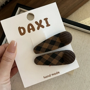 Détail d'une pince à cheveux à nœud à carreaux marron sur son support en carton