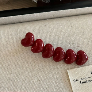 Eleganter roter Haarclip in Herzform mit Perlen auf einem cremefarbenen Hintergrund