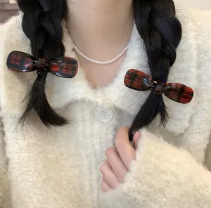 Detail of red plaid bow hair clips worn on a dark braid with a pearl necklace accent