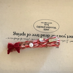 Knitted hair clip with red bow, pearl, and rhinestone heart on a beige background