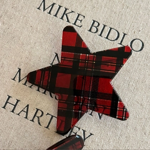 Star-shaped red and black plaid bow hair clip on a textured beige linen background