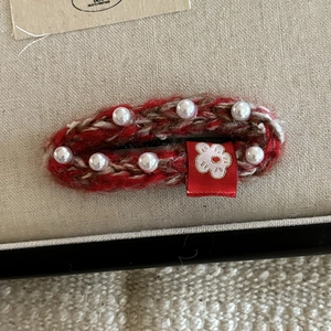 Detail of red knitted hair clip with white faux pearls and a small embroidered flower motif