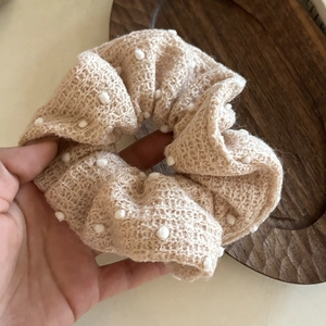 Chic beige polka dot knit scrunchie for low ponytail styling on a wooden tray