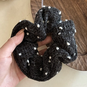 Close-up of a black knitted polka dot hair scrunchie with thick fluffy wool texture