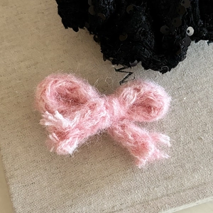 Gros plan d'une pince à cheveux nœud en tricot rose montrant la texture douce du fil