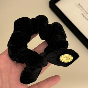 Elegant black velvet scrunchie with bow tie and golden oval metal brand label