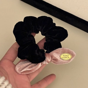 Close-up of velvet bow hair tie featuring a polished gold metal logo tag and soft texture