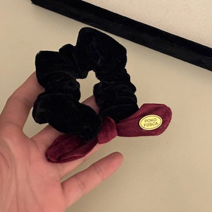 Close-up of black velvet scrunchie with dark red corduroy bow and gold metal logo charm