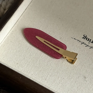 Gros plan d'une pince à cheveux bordeaux scintillante avec base dorée sur un fond doux beige