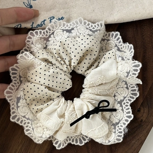 Vintage lace scrunchie with beige polka dots and a small black bow on wood surface